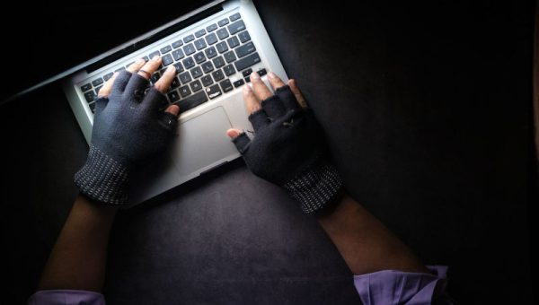 Corporate worker in gloves on laptop, possibly engaging in financial crimes.